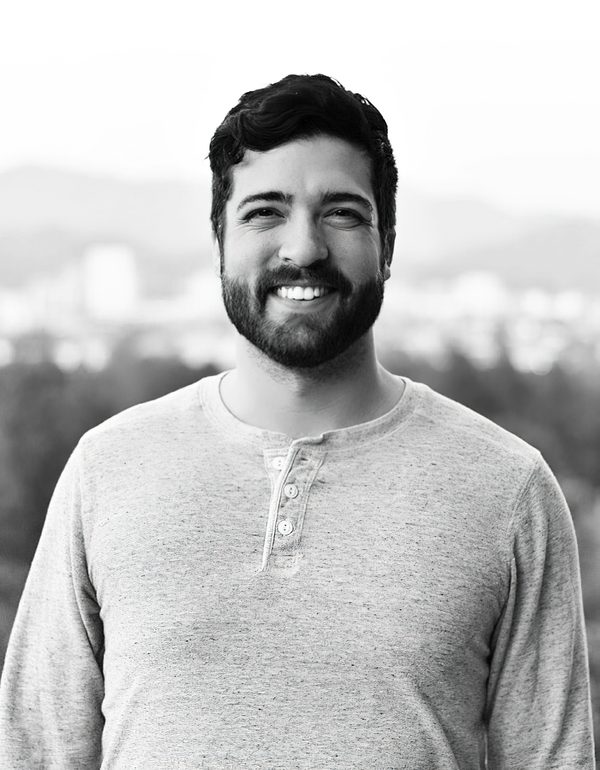 David Ridd, smiling, in a grey henley with a city skyline out of focus behind him